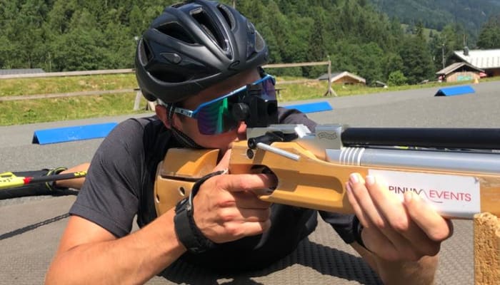 Athlète en biathlon tenant un fusil de tir couché avec montagne et forêt en arrière-plan
