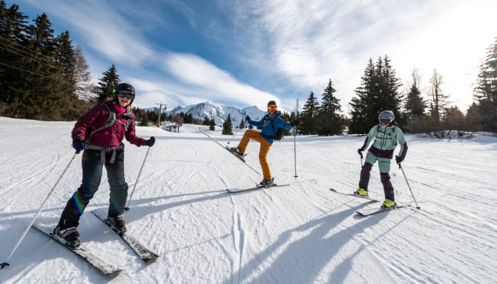 Trois skieurs en action sur une piste enneigée avec montagnes enneigées et forêts de sapins en arrière-plan