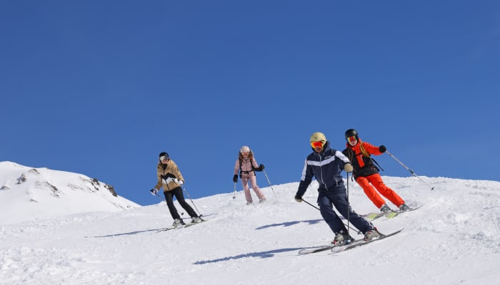 Groupe de jeunes skieurs en cours collectif sur les pistes enneigées des Arcs sous ciel bleu