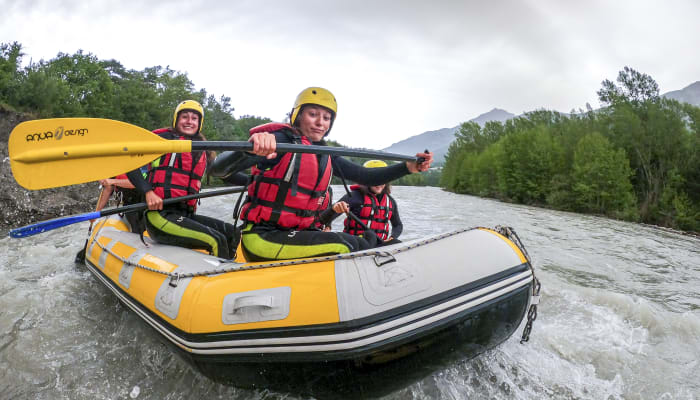 Groupe de rafters en gilet de sauvetage rouge et jaune naviguant en raft sur une rivière en montagne lors d'une activité Multisport Audace