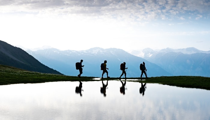 Groupe de randonneurs en itinérance dans les Écrins avec sommets enneigés et lac alpin en réflexion