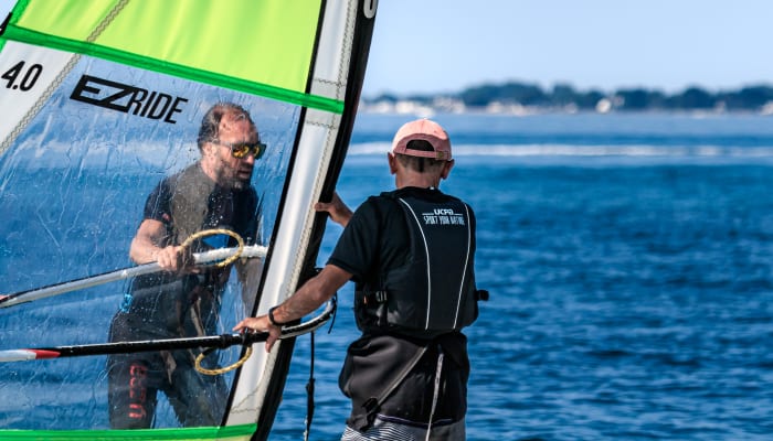 Moniteur de windsurf accompagnant un élève sur une planche avec voile verte en Bretagne face à l'océan
