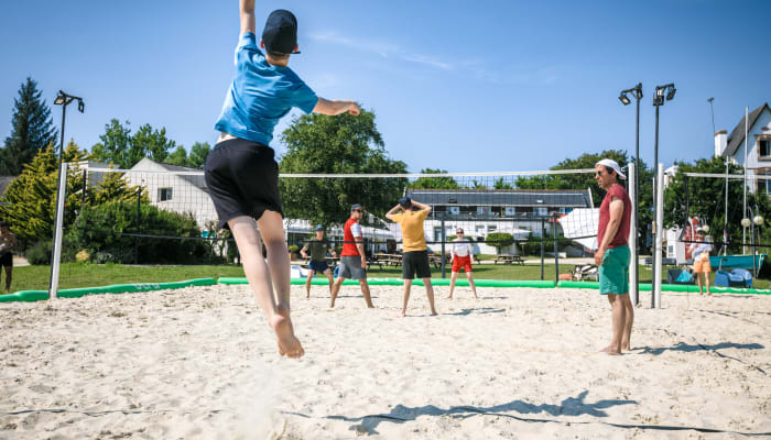 Joueur de volley-ball sautant pour frapper le ballon sur un terrain de sable à Bénodet-Glénan, avec d'autres participants et filets en arrière-plan