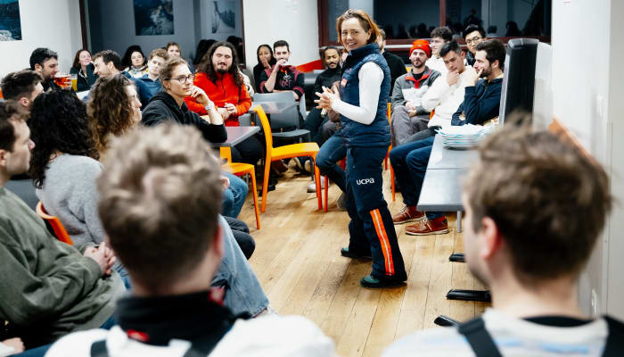 Groupe de jeunes adultes réunis dans une salle pour la semaine Fresh Fresh Week, animateur en gilet bleu présentant le programme snowboard à Chamonix