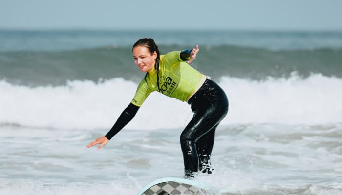 Surfeur en combinaison jaune et noire glissant sur une vague aux Landes avec technique équilibrée