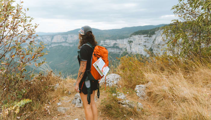 Randonneuse avec sac à dos orange face aux falaises spectaculaires du massif du Vercors