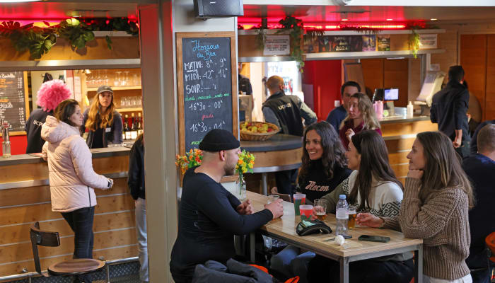 Intérieur animé d'un bar-restaurant des Arcs avec clients assis à des tables, comptoir de service et menu affiché