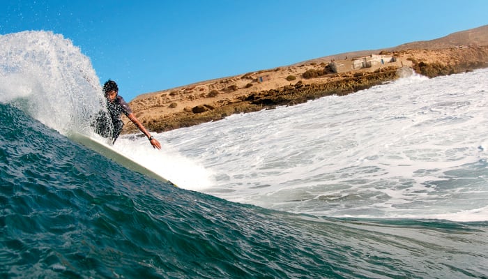 Surfeur sur une vague parfaite à Taghazout avec côte rocheuse marocaine et ciel bleu