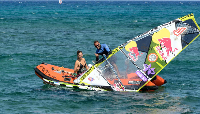 Windsurfeur et instructeur en mer avec voile colorée et planche de windsurf dans une baie aux eaux turquoise