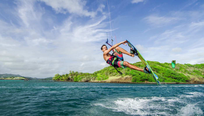 Kitesurfeur en action avec voile verte sur les eaux turquoise de la Martinique avec côte verdoyante en arrière-plan