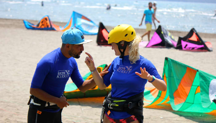 Moniteurs de kitesurf en équipement de sécurité discutant sur la plage avec cerfs-volants colorés et autres stagiaires en arrière-plan