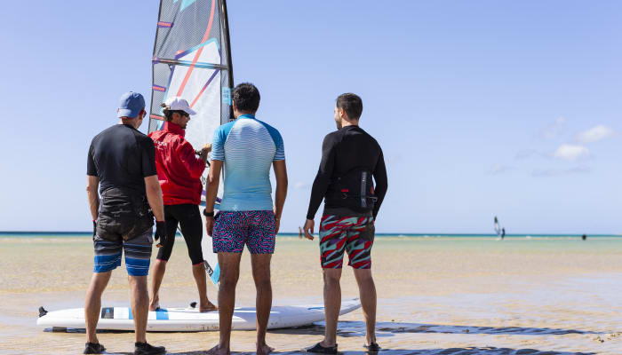 Groupe de windsurfeurs sur la plage préparant leur matériel avec voile colorée et planche avant de prendre la mer
