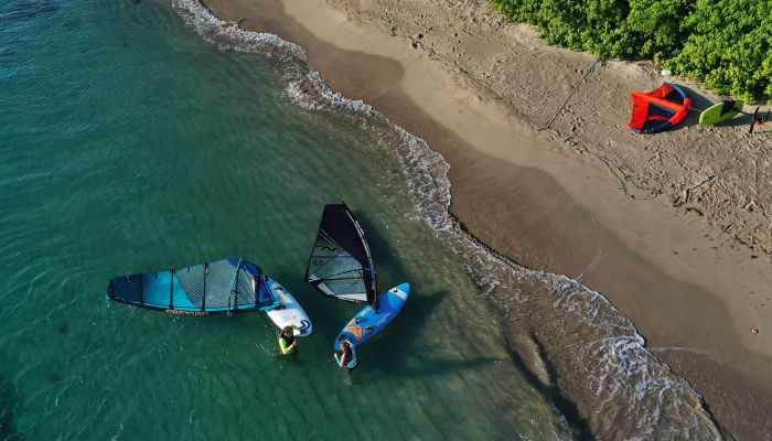 Planche à voile et équipement de windsurf sur plage de sable avec eaux turquoises et végétation tropicale
