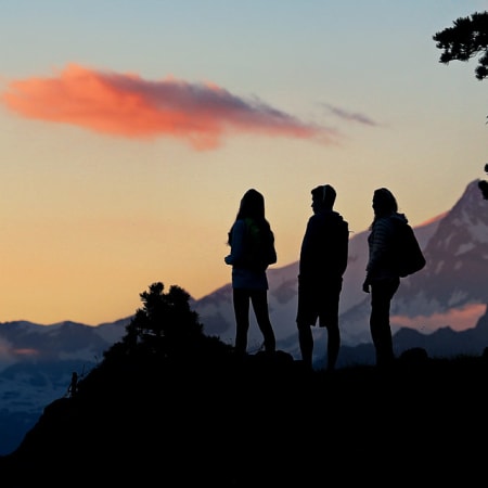 Trois randonneurs en silhouette au coucher de soleil face aux sommets alpins du Grand Paradis
