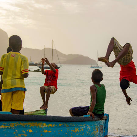 Enfants jouant sur une plage de Santa Antão au Cap Vert avec montagnes volcaniques et voiliers en arrière-plan