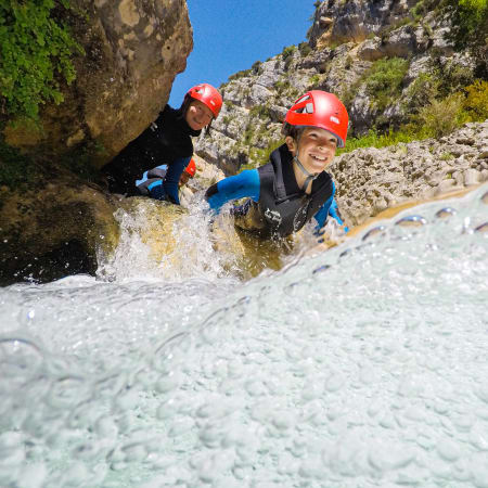 Enfants en canyoning portant casques rouges traversant un ruisseau entre les parois rocheuses du canyon