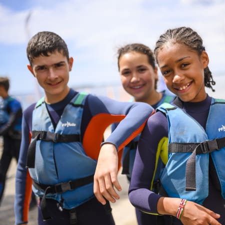 Groupe de jeunes en combinaison néoprène et gilet de sauvetage prêts pour une session de windsurf et wingsurf en mer