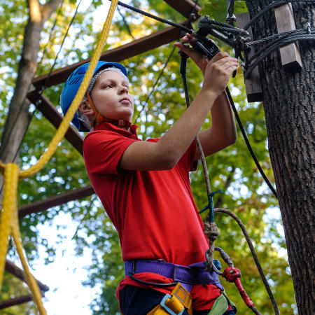 Enfant en équipement de sécurité pratiquant l'escalade en parc aventure multisports