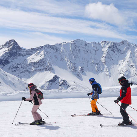 Trois skieurs en action sur les pistes enneigées de La Plagne avec chaîne de montagnes enneigées en arrière-plan