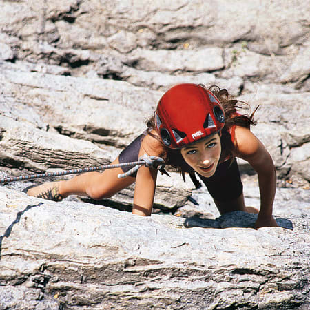 Jeune grimpeur en casque rouge escaladant une paroi rocheuse en altitude, technique alpinisme