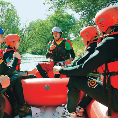 Groupe de jeunes en gilets de sauvetage et casques rouges préparant un rafting en eaux vives à Serre Chevalier
