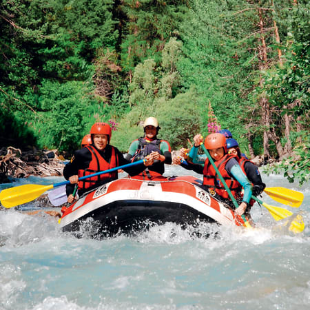 Groupe de participants en rafting équipés de casques et gilets de sauvetage naviguant dans les rapides d'une rivière de montagne