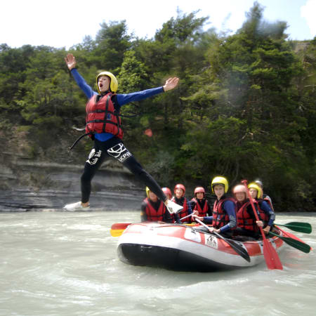 Adolescent en gilet de sauvetage rouge sautant au-dessus d'un radeau avec groupe de jeunes pratiquant le rafting en rivière aux Orres