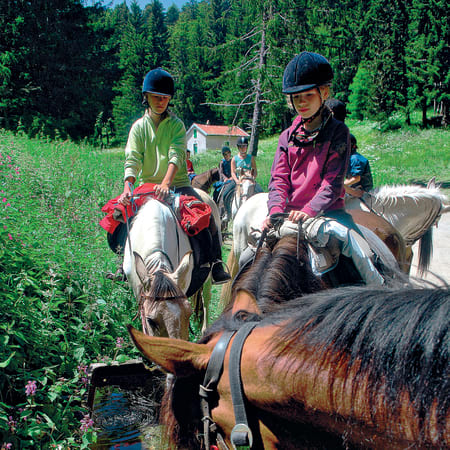 Deux jeunes cavaliers à cheval dans les paysages verdoyants du Vercors lors d'un raid équestre en montagne