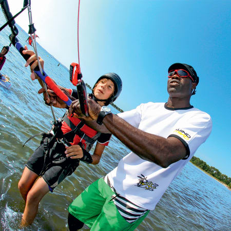 Moniteur de kitesurf enseignant à un élève équipé de harnais et voile rouge aux Caraïbes sous ciel bleu