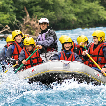 Groupe de jeunes en rafting sur eau turquoise avec casques et gilets de sauvetage pour activité multisports en montagne