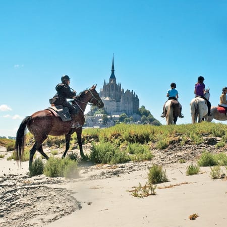 Cavaliers à cheval dans la baie du Mont-Saint-Michel avec vue sur l'abbaye médiévale, séjour équestre jeunes