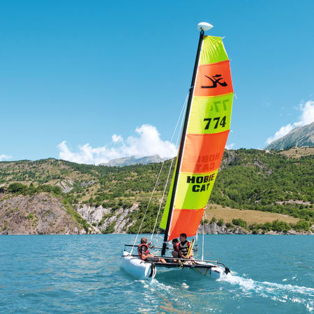 Catamaran de kitesurf coloré aux voiles rouges et jaunes naviguant sur un lac alpin aux Crots avec montagnes en arrière-plan
