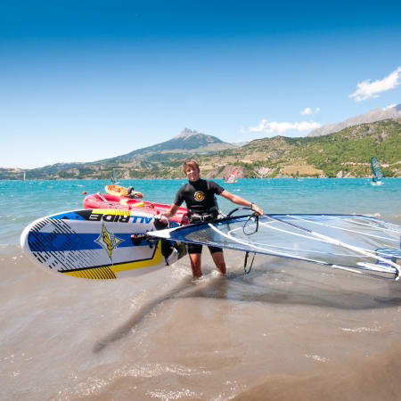 Adolescent avec équipements de voile et kitesurf sur une plage entre rivière et lac en montagne