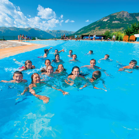 Groupe de jeunes en séjour multisports nageant dans une piscine olympique aux Orres avec montagnes en arrière-plan
