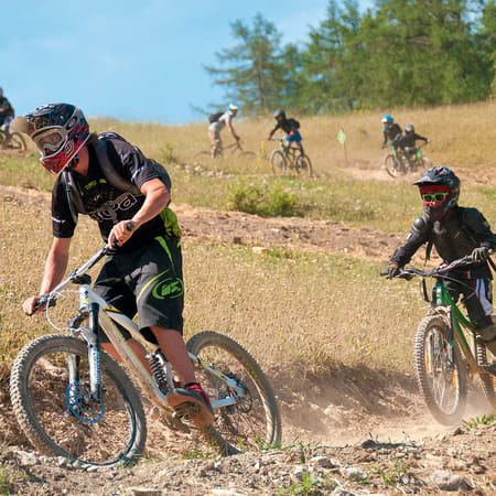Jeune cycliste en VTT freeride sur terrain accidenté avec groupe d'enfants pratiquant le VTT en arrière-plan dans un cadre naturel ensoleillé