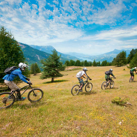 Groupe de jeunes pilotes en VTT freeride dans une vallée alpine avec montagnes boisées en arrière-plan