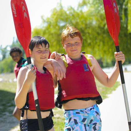 Deux enfants souriant en tenue rouge tenant des pagaies lors d'activités multisports en forêt