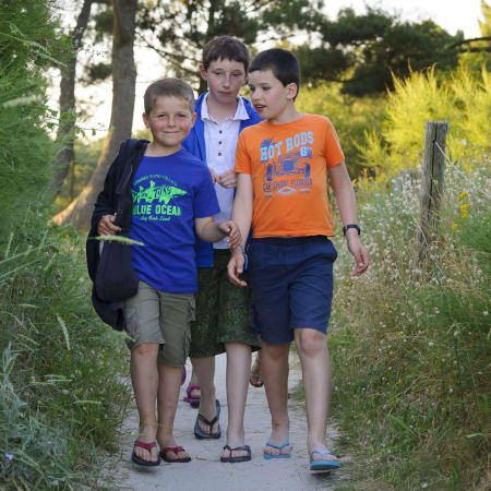 Trois enfants marchent ensemble sur un sentier en Bretagne pendant une colonie de vacances surf