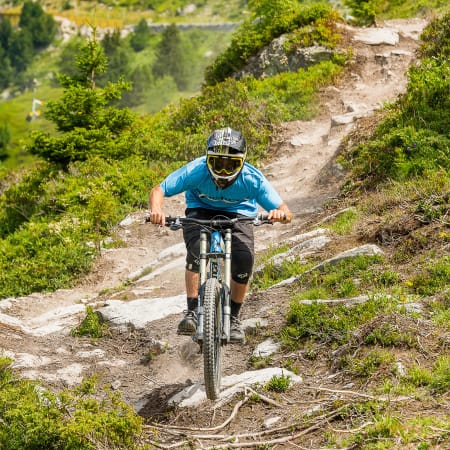 Jeune cycliste en descente VTT sur sentier montagneux aux Arcs avec casque et maillot bleu