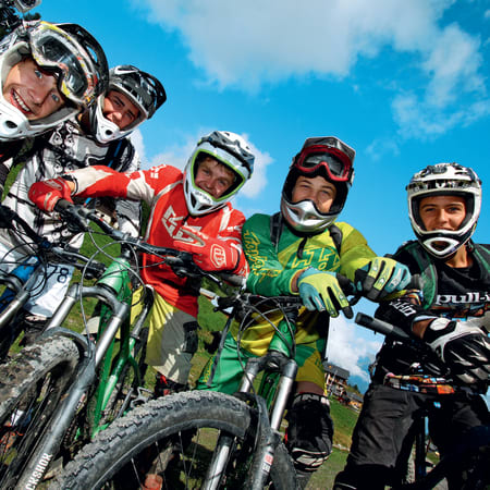 Groupe de pilotes VTT descente en équipement de protection complet posant avec leurs vélos en montagne sous le soleil