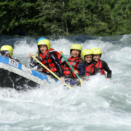 Groupe de jeunes en rafting dans les eaux vives avec casques jaunes et gilets de sauvetage rouges