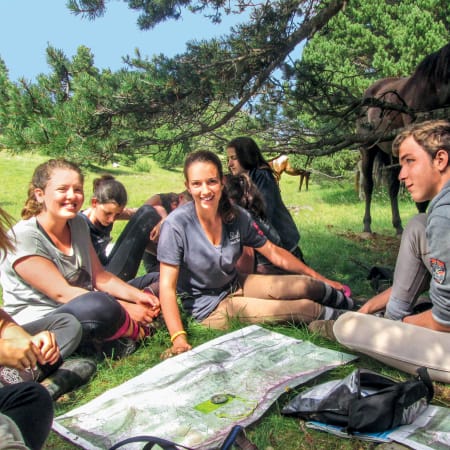 Groupe de jeunes cavaliers en pause sous un arbre lors d'un séjour itinérant équestre au Parc du Vercors, consultant une carte