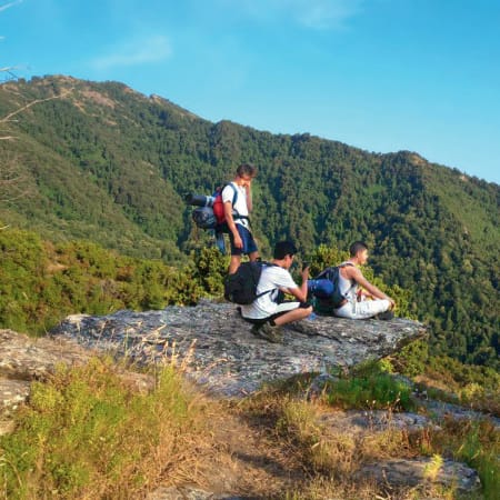 Jeunes randonneurs en montagne corse avec vue panoramique sur les vallées boisées et mer en arrière-plan
