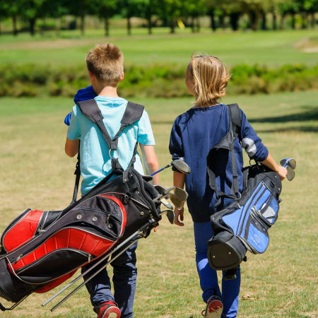 Deux enfants de 8-10 ans marchant dans un parc avec leurs sacs de golf multisports sous le bras
