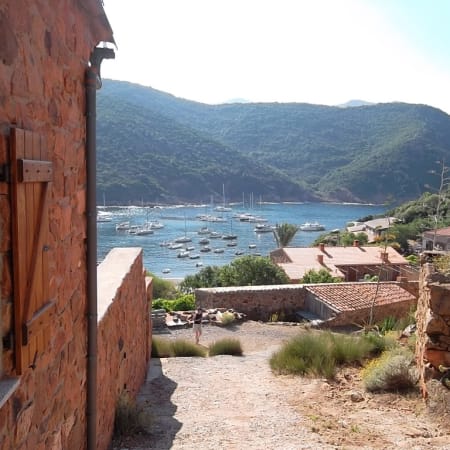 Baie de Scandola en Corse avec voiliers mouillés, montagnes boisées et village côtier pittoresque