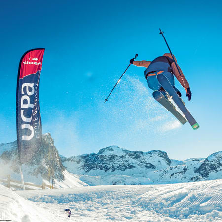 Skieur en l'air effectuant un saut freestyle dans un terrain enneigé aux Orres avec montagnes en arrière-plan
