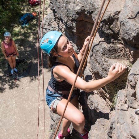Grimpeur en escalade sur paroi rocheuse avec casque bleu, encordé et assuré par un moniteur UCPA