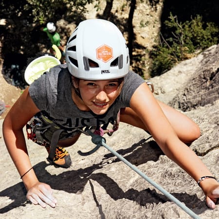 Jeune adolescent en escalade sportive portant casque et baudrier sur paroi rocheuse pour séjour multisports en montagne