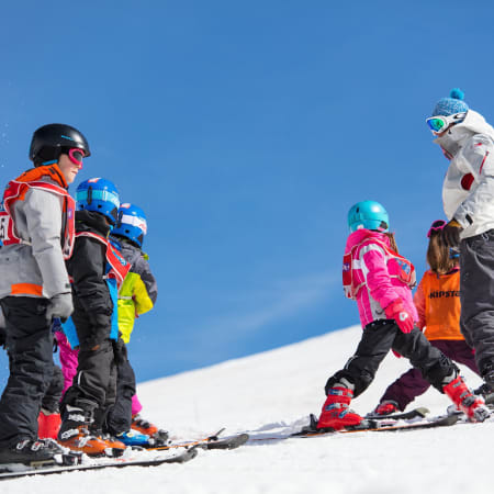 Groupe d'enfants en cours de ski avec moniteur sur piste enneigée en montagne sous ciel bleu