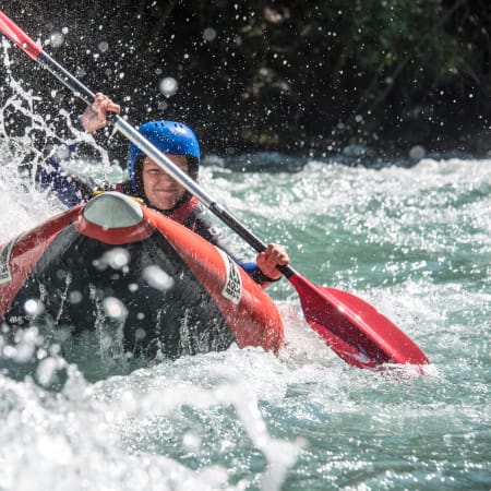 Jeune kayakiste en embarcation individuelle naviguant des rapides classe III avec pagaie rouge et casque bleu